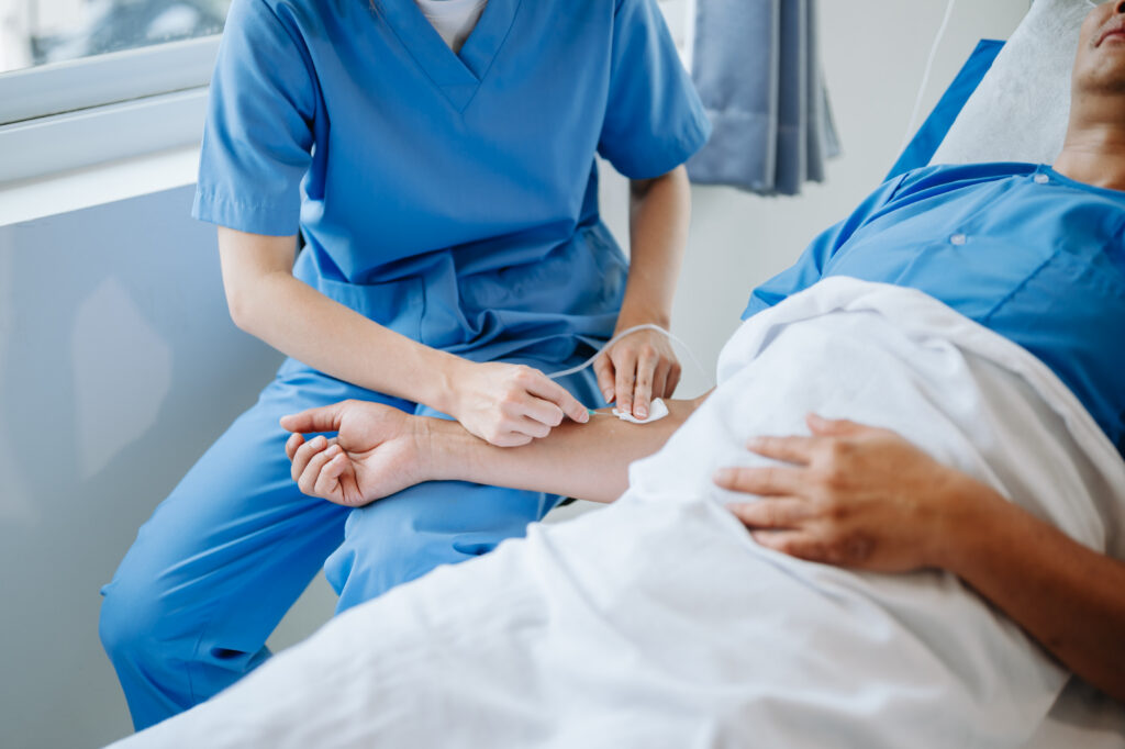 Friendly Female Head Nurse Making Rounds does Checkup on Patient Resting in Bed. She Checks tablet while Man Fully Recovering after Successful Surgery in a hospital