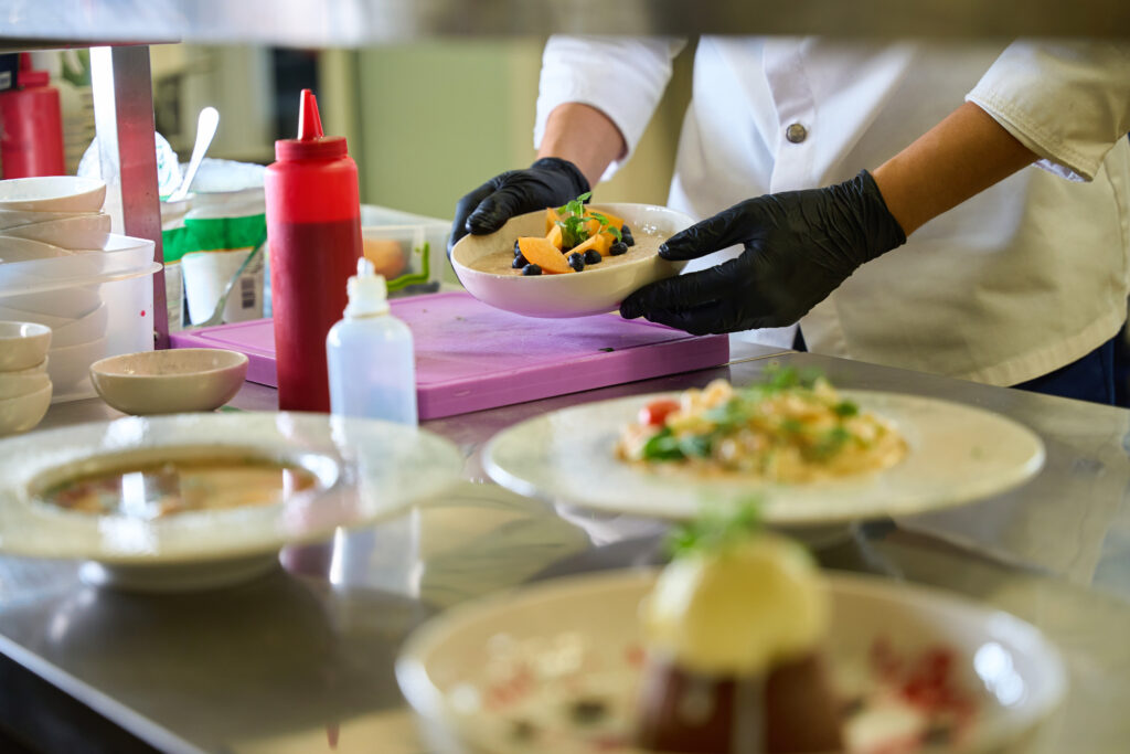 Cook decorates ready-made dishes for serving, he works wearing protective gloves