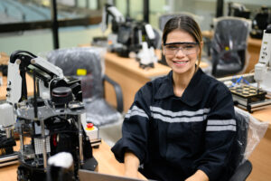 Female technician engineer using laptop checking and operating automatic robotic machine at industrial factory, Worker working with robotic system in factory